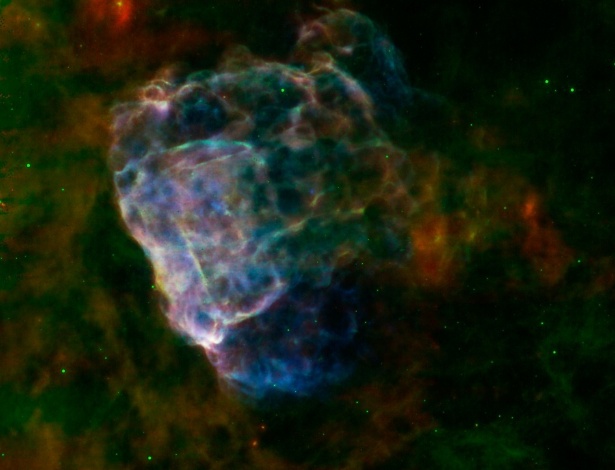 Imagem feita a partir de uma supernova captada pela Nasa e pela Agência Espacial Europeia mostra nuvem de poeira colorida. Informação em infravermelho do fotômetro de imagem do telescópio Spitzer, da Nasa, em ondas de 24 e 70 microns surgem em vermelho e verde e raios X do XMM-Newton em um alcance de 0.3 a 8 kiloelectron volts em azul