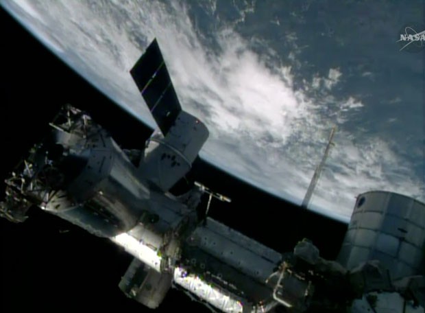 Imagem da Nasa TV mostra a cápsula de abastecimento Dragon acoplada à Estação Espacial Internacional neste domingo (20) (Foto: NASA-TV/AP)