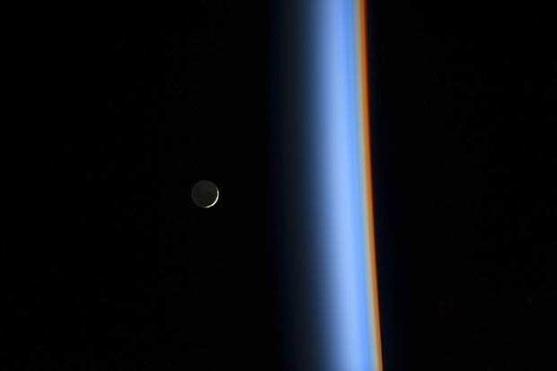 Lua crescente é vista à esquerda, ao lado da luz que atravessa a atmosfera em cores diferentes à direita (Foto: Koichi Wakata/Nasa/Reuters)