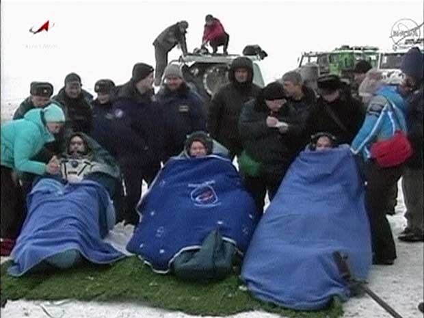 Cosmonautas russos e astronauta americano são aquecidos por cobertores logo após pouso da Soyuz nas estepes do Cazaquistão. (Foto: Nasa TV / Reuters)