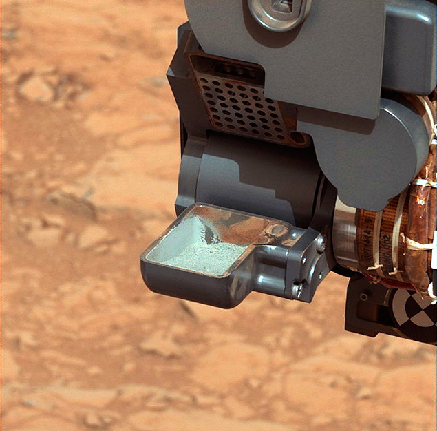 O jipe-robô Cusiosity mostra um pó cinza, a primeira amostra de solo perfurado coletada em Marte, que permitiu a descoberta dos elementos químicos básicos para existência de vida 