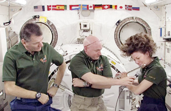 Astronauta Scott Kelly (centro) segura microfone para a colega Catherine Coleman (dir.), que toca flauta