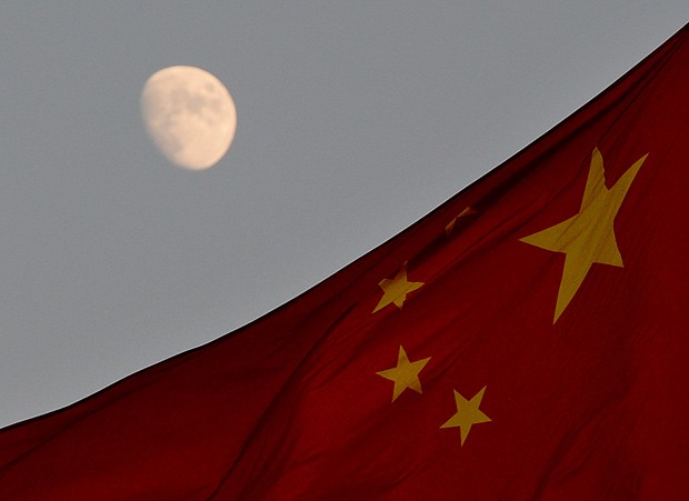 Bandeira chinesa é vista em frente à lua na Praça Tiananmen, em Pequim, nesta sexta-feira (13); veículo lunar chinês deve pousar na Lua neste sábado. (Foto: AFP Photo/Mark Ralston)